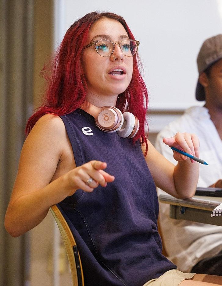 a student with bright red hair and headphones takes part in a class discussion. 